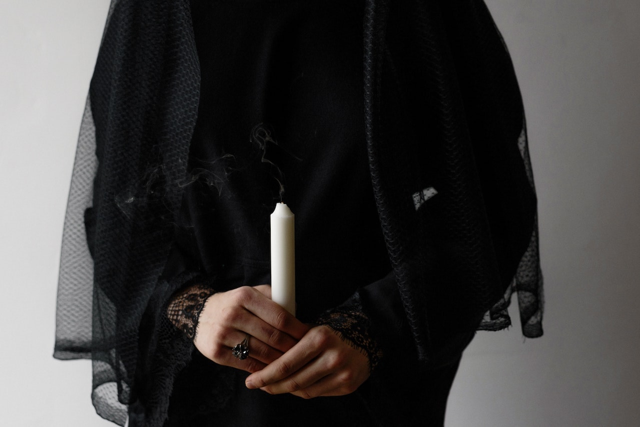 Person in Black Veil Holding White Candle