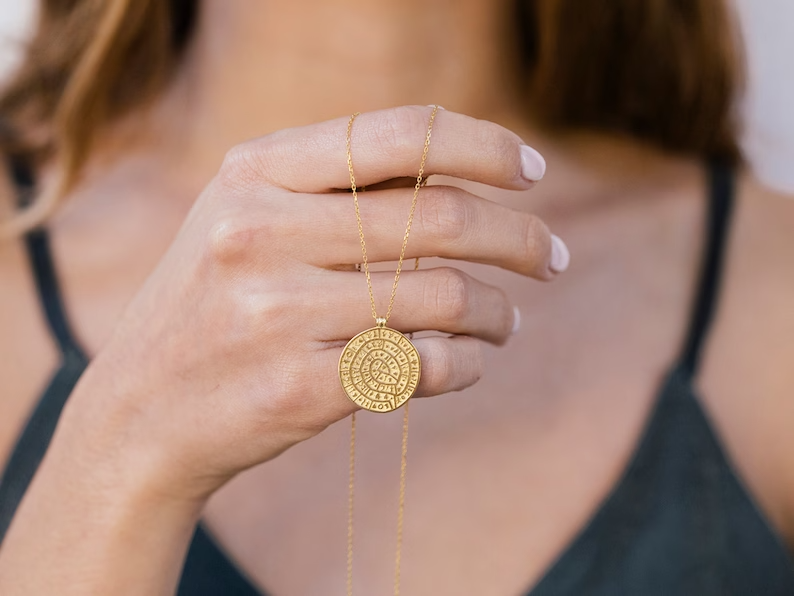 a woman holding a gold phaistos disk pendant necklace