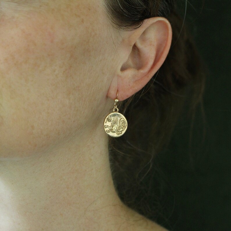 a woman wearing a gold simurgh design earring
