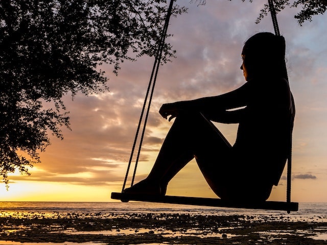 a woman on a swing looking at sunset