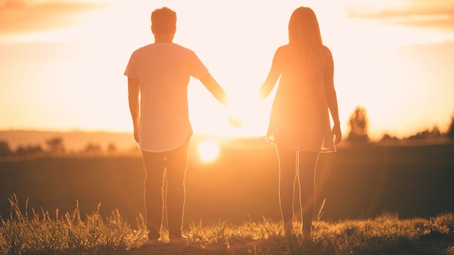 Man and a woman holding hands facing the sunset