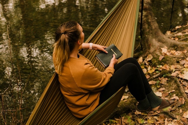 a woman holding a bible and sitting on a hammock
